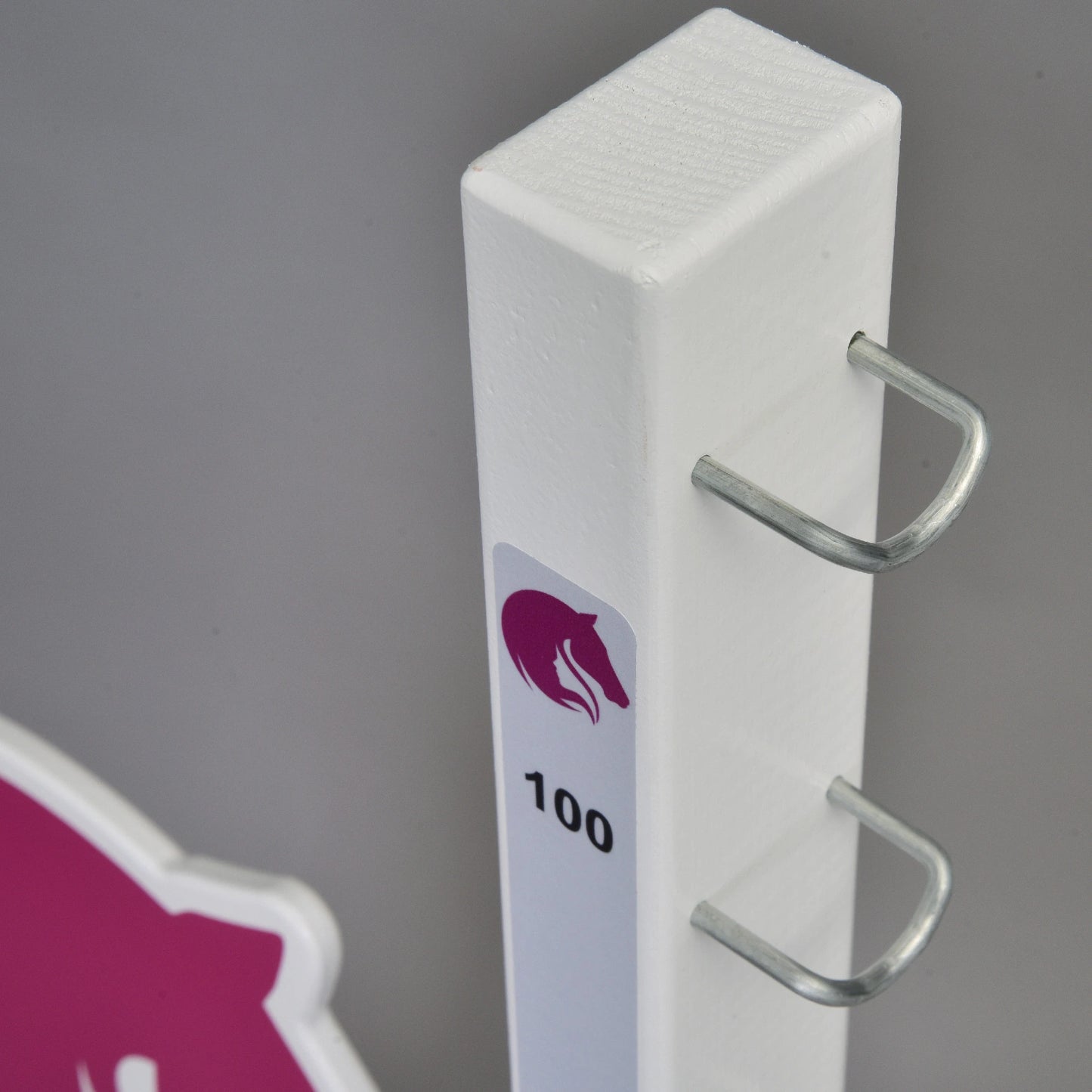Poteau vertical blanc de Hobby Horse LarDen, marqué « LarDen jump 110 cm / 43 inch », avec deux crochets métalliques, une icône de tête de cheval violette et le nombre 100, suggérant un obstacle réglable pour Hobby Horse. Un panneau rose et blanc apparaît en arrière-plan.