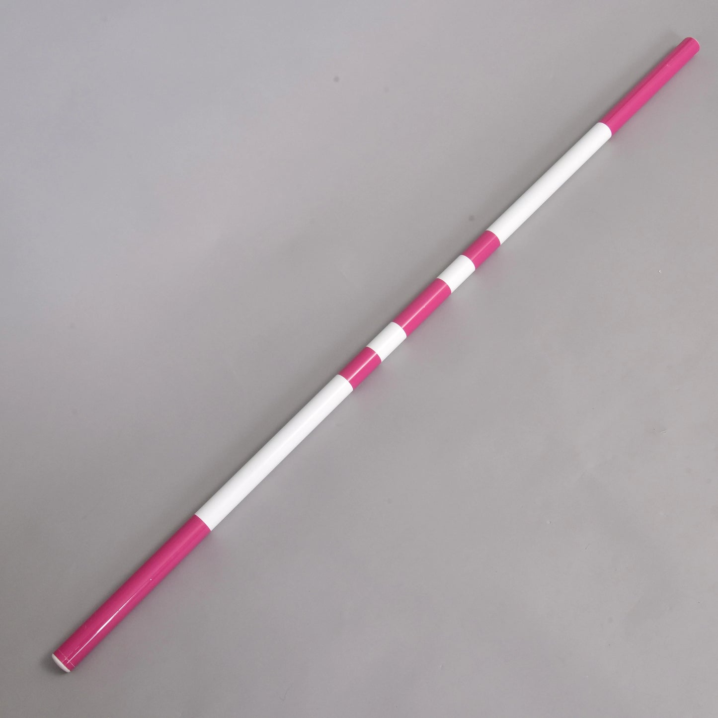 Die Jump pole pink von Hobby Horse LarDen mit abwechselnd rosa und weißen Segmenten ist diagonal auf einer schlichten grauen Oberfläche dargestellt.