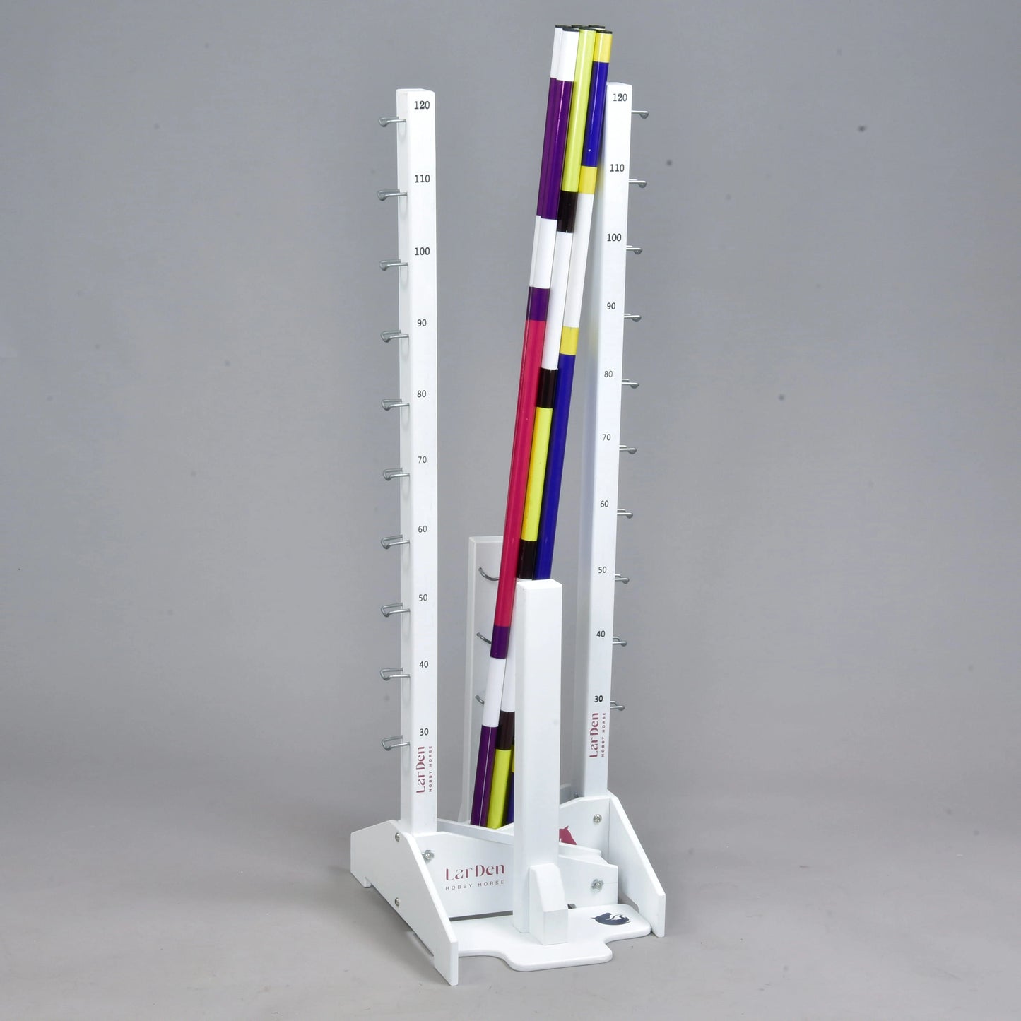 Hindernis Set für Hobby Horsing von Hobby Horse LarDen mit einem senkrechten weißen Ständer mit Höhenmarkierungen und farbigen gestreiften Stangen in Lila, Gelb, Weiß und Schwarz – ideal als Hindernis oder verstellbares Cavaletti. Der Hintergrund ist schlicht grau.