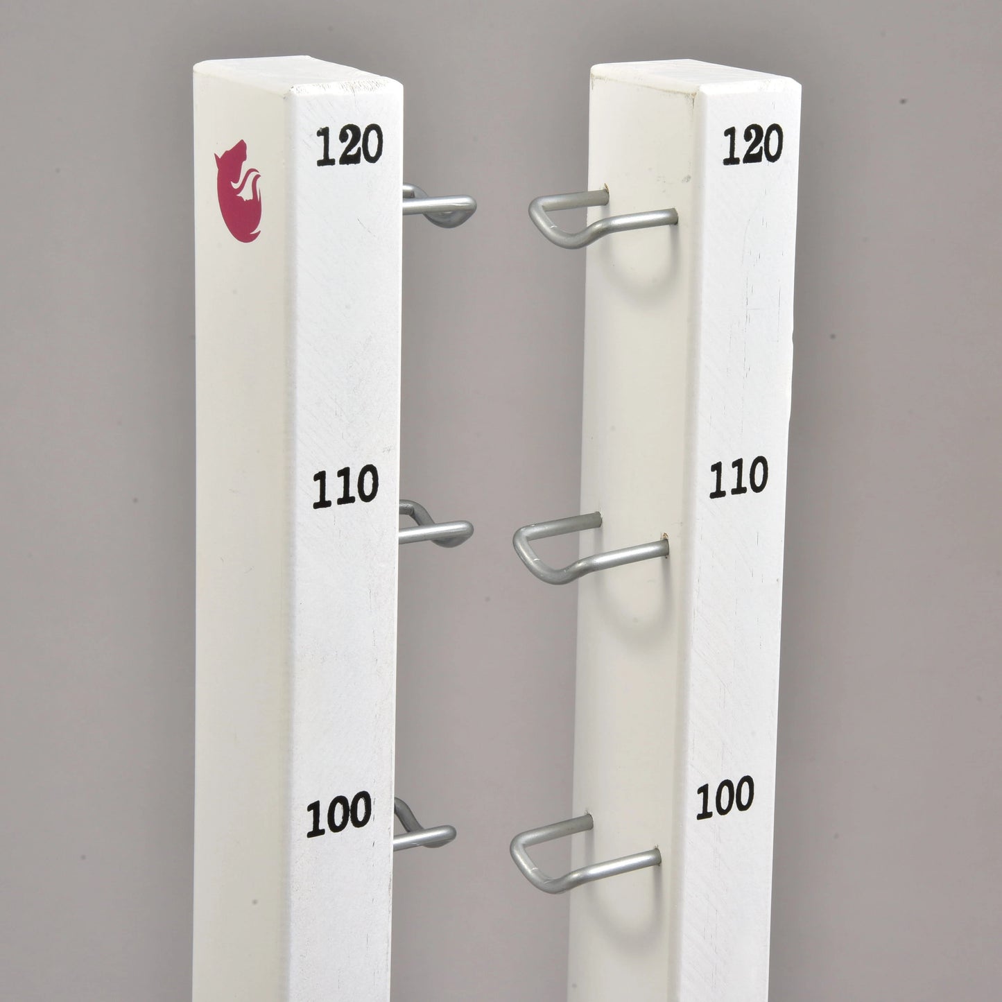 Hindernis Set für Hobby Horsing von Hobby Horse LarDen mit zwei weißen senkrechten Pfosten mit Metallhalterungen auf den Höhen 100, 110 und 120, ideal als Hindernis oder Cavaletti. Der linke Pfosten ist oben mit einem roten Fuchs-Logo versehen. Hintergrund in schlichtem Grau.