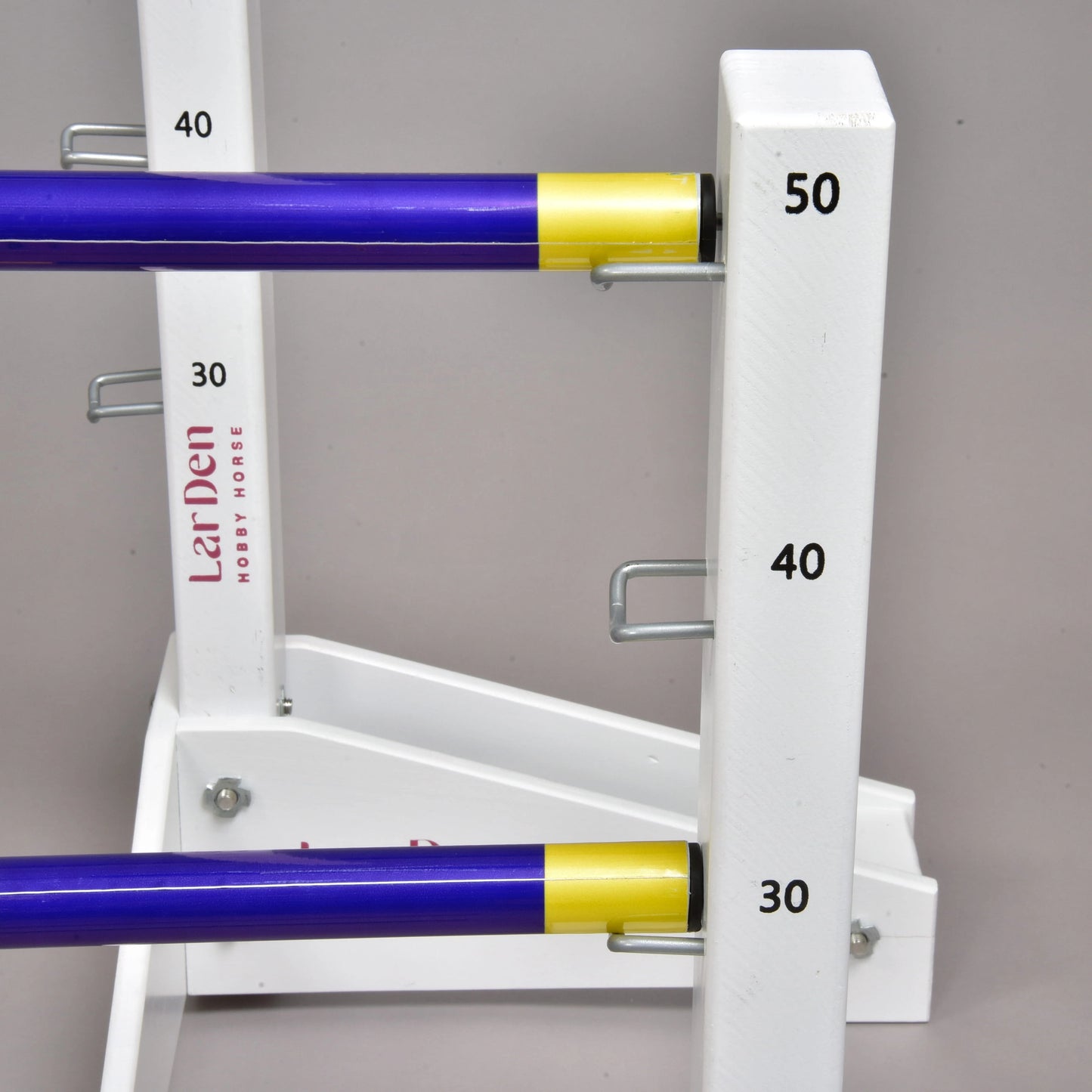Hindernis Set für Hobby Horsing von Hobby Horse LarDen, Nahaufnahme mit weißen Ständern und lila sowie gelben Stangen in unterschiedlichen Höhen, markiert mit 30, 40 und 50. Metallhaken sichern die verstellbaren Stangen – ideal für Hobby Horsing Fans.