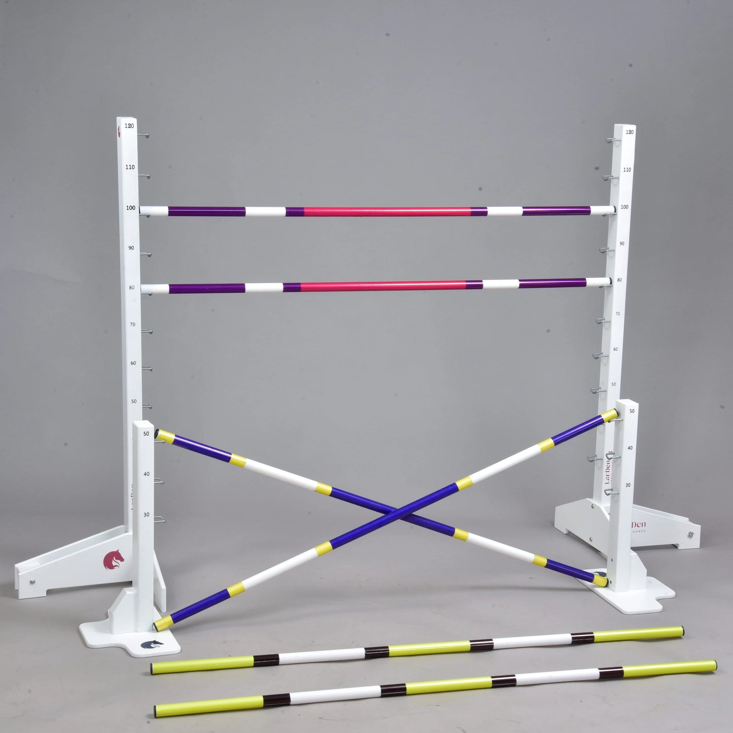 Hindernis Set für Hobby Horsing von Hobby Horse LarDen mit weißen Ständern mit Höhenmarkierungen, vier farbigen Stangen (zwei waagerecht und zwei gekreuzt) sowie zwei gelb-schwarzen Cavaletti davor, gezeigt vor schlichtem grauem Hintergrund.