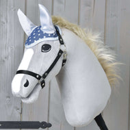 Plüsch-Hobby Horse von Hobby Horse LarDen mit weißem Gesicht, schwarzem Zaumzeug, blauer Ohrenkappe Star mit Sternenmuster zum Fliegenschutz, heller Mähne und Cartoon-Augen, vor Holz-Hintergrund.