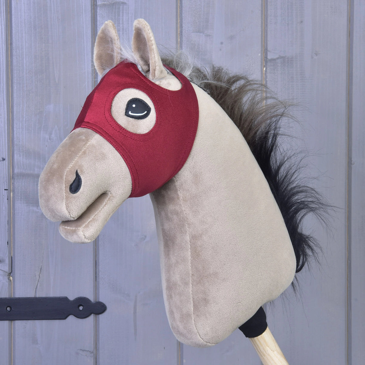 Eine samtige Pferdemaske ohne Ohren von Hobby Horse LarDen auf einem Holzstab vor grauer Holzvertäfelung, ein waschbares Spielzeug für fantasievolles Spielen und einfache Pflege