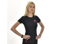 Eine junge Frau mit langen blonden Haaren steht vor weißem Hintergrund und trägt das Hobby Horse LarDen "T-Shirt LarDen Active Black" mit rosa Logo und Akzenten. Sie posiert mit den Händen in den Hüften und hebt das Spandex-Material und die Armbänder hervor.