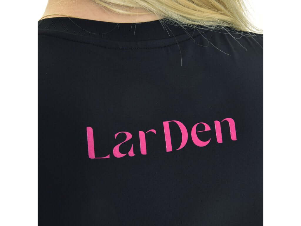 Nahaufnahme der Rückseite eines T-Shirt LarDen Active Black von Hobby Horse LarDen mit auffälligem pinkem „LarDen“-Schriftzug. Blonde Haare bedecken den oberen Teil des Shirts teilweise.