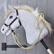 Hobby Horse LarDen Westernzügel Dakota, ein graues Hobby Horse mit blonder Mähne, schwarzem Zaumzeug und gelbem Seil mit Karabinerhaken, hängt an einer Holzwand in einer schwarzen Halterung – ideal als Trainingszügel.