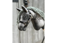Nahaufnahme von Hobby Horse Bentley mit schwarzem Halfter von Hobby Horse LarDen in Größe XS mit grauem Stoffkopf, schwarzem Halfter, Knopfaugen und Garnmähne vor verschwommenem Holz-Hintergrund.