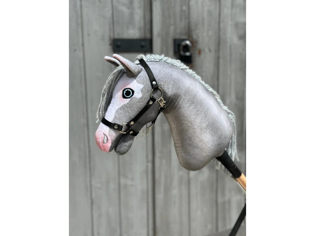 The Hobby Horse LarDen Midnight Blue with Black Halter (size S) is mounted on a wooden stick and displayed in front of a weathered wooden door.