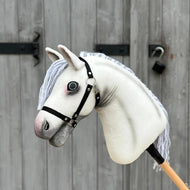 Hobby Horse Atlas mit schwarzem Halfter von Hobby Horse LarDen mit weißem Appaloosa-Design und grauer Garnmähne vor einer Holztür mit Metallriegel und Vorhängeschloss.