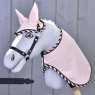 Set Abby von Hobby Horse LarDen ist ein grau-weißes Stoff-Hobby Horse mit Plüschmähne, gesticktem Auge und rosa Zaumzeug- und Deckenset, dargestellt vor einer hellen Holzwand.