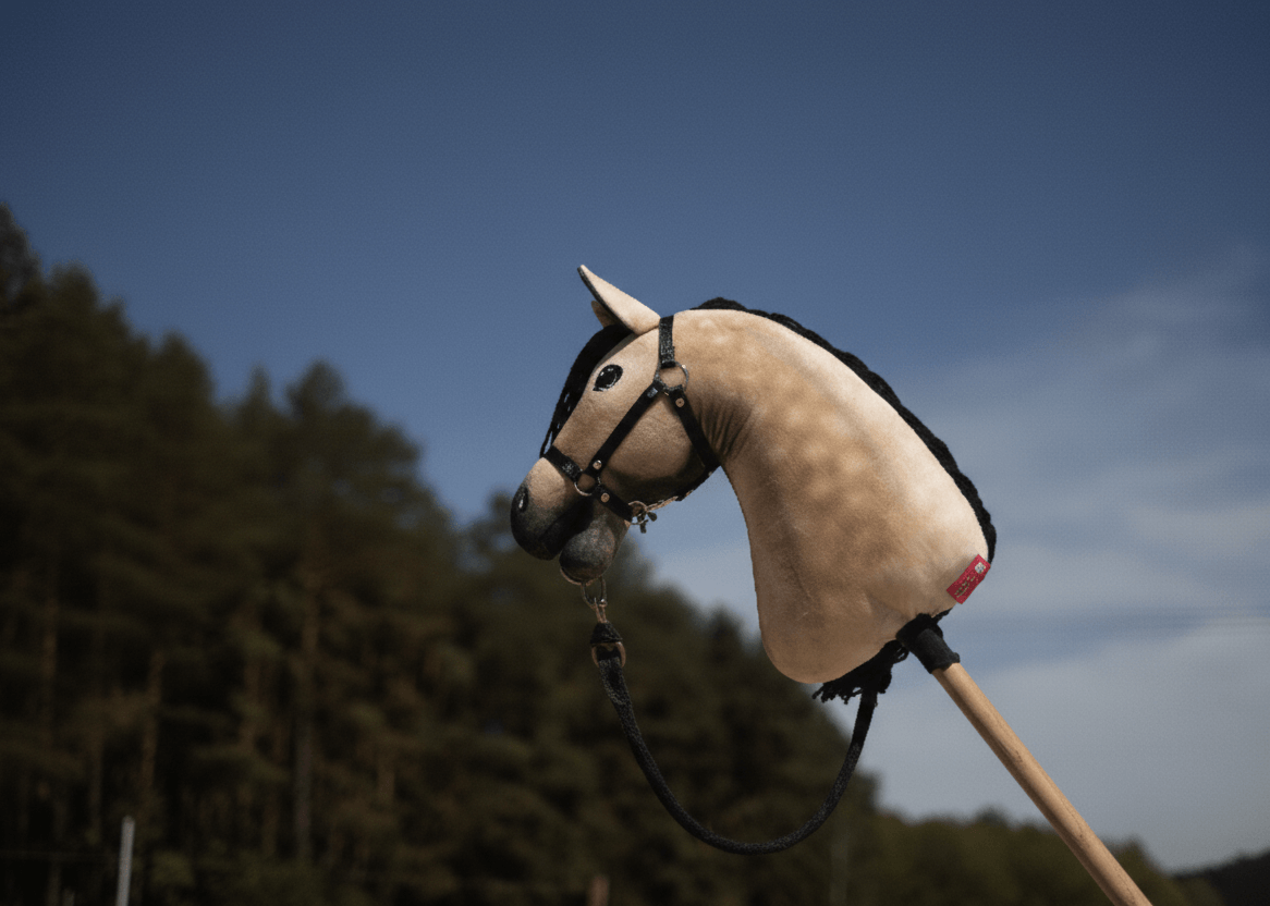 Ein Hobby Horse-Spielzeug mit Stoffpferdekopf und schwarzer Mähne wird im Freien vor klarem blauem Himmel und hohen grünen Bäumen hochgehalten – eine perfekte Szene für alle Hobby Horsing-Begeisterten.