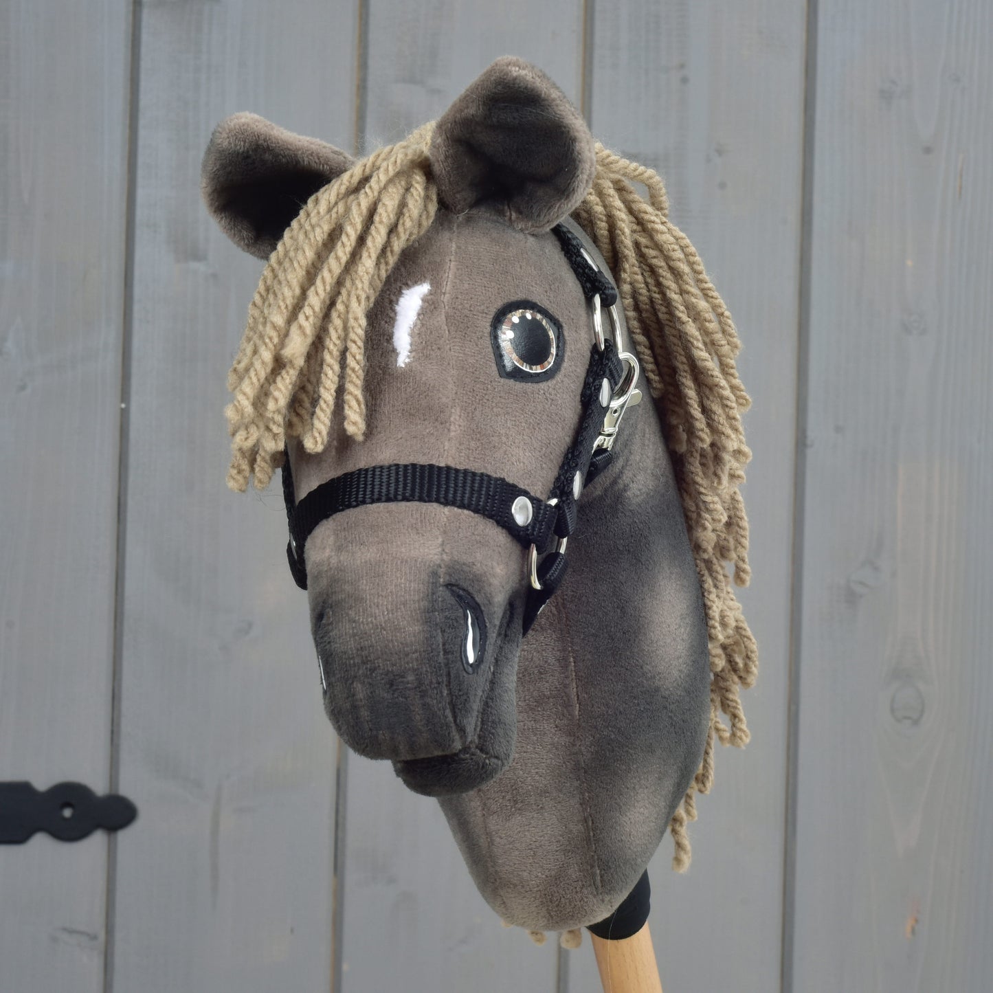 Hobby Horse Avalon mit schwarzem Halfter, Größe XS von Hobby Horse LarDen mit braunem Plüschkopf, schwarzem Halfter und Garnmähne, inspiriert von einem englischen Warmblut-Sportpferd, vor Holzbackground