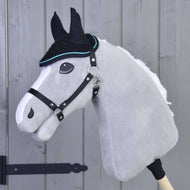 Die Ohrenkappe gehäkelt Blackie von Hobby Horse LarDen ist auf einem grauen Hobby Horse mit schwarzem Zaumzeug zu sehen, auf einem Holzstab montiert und vor einer grauen Holzwand.