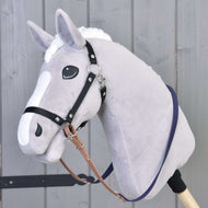 Ein Plüsch-Hobby Horse von Hobby Horse LarDen mit hellgrauem Kopf, weißer Mähne und Gesichtszeichnung trägt die Gummierte Zügel - Brown Purple. Es steht vor einer Holzwand.