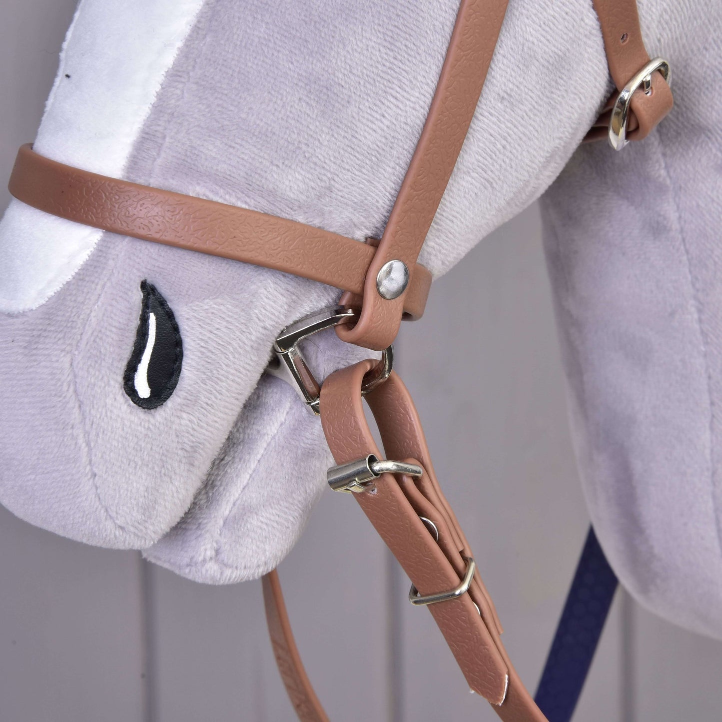 Nahaufnahme eines Plüsch-Pferdekopfspielzeugs von Hobby Horse LarDen mit dem Komplettes Zaumzeug mit Nasenriemen Brown Purple und einem gestickten schwarz-weißen tränenförmigen Auge.