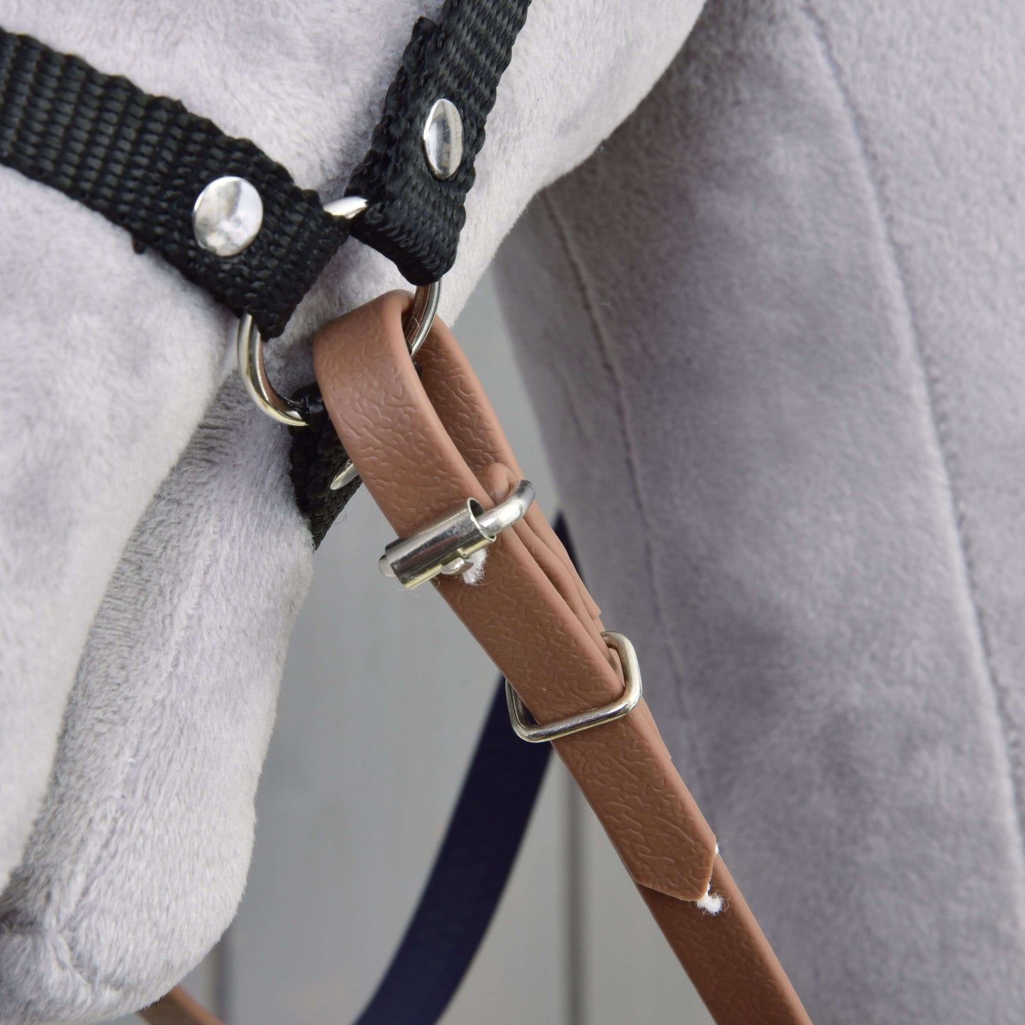 Gros plan sur une peluche douce gris clair portant les Rênes caoutchoutées marron violet de Hobby Horse LarDen : une bride sans mors avec harnais à sangles noires, anneaux métalliques et lanière en simili cuir marron.