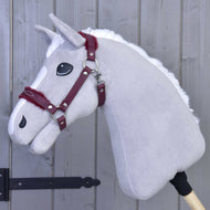 Halfter mit Fell - Kunstleder Burgundy von Hobby Horse LarDen, gezeigt an einem grauen plüschigen Hobby Horse mit weißer Mähne und kastanienrotem Zaumzeug, verleiht vor einer grauen Holzwand einen stilvollen Akzent – das perfekte Accessoire.
