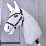 The Hobby Horse LarDen gray plush hobby horse features the crocheted Nicol red ear bonnet, a bridle, and a straw hat, mounted on a wooden stick and displayed in front of a wooden plank background.