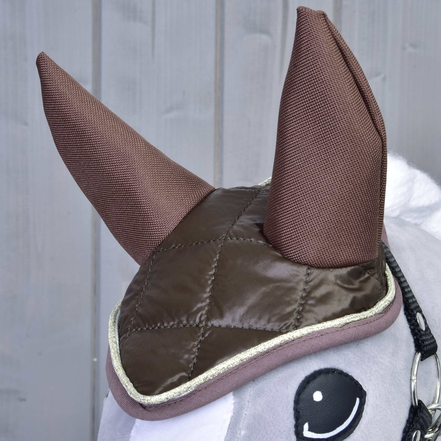 Gros plan sur l’Ensemble Thermo Chocolat de Hobby Horse LarDen montrant ses grandes oreilles en tissu et son bonnet d’oreilles matelassé marron avec bordure claire, décoration de cheval charmante sur fond en bois gris.