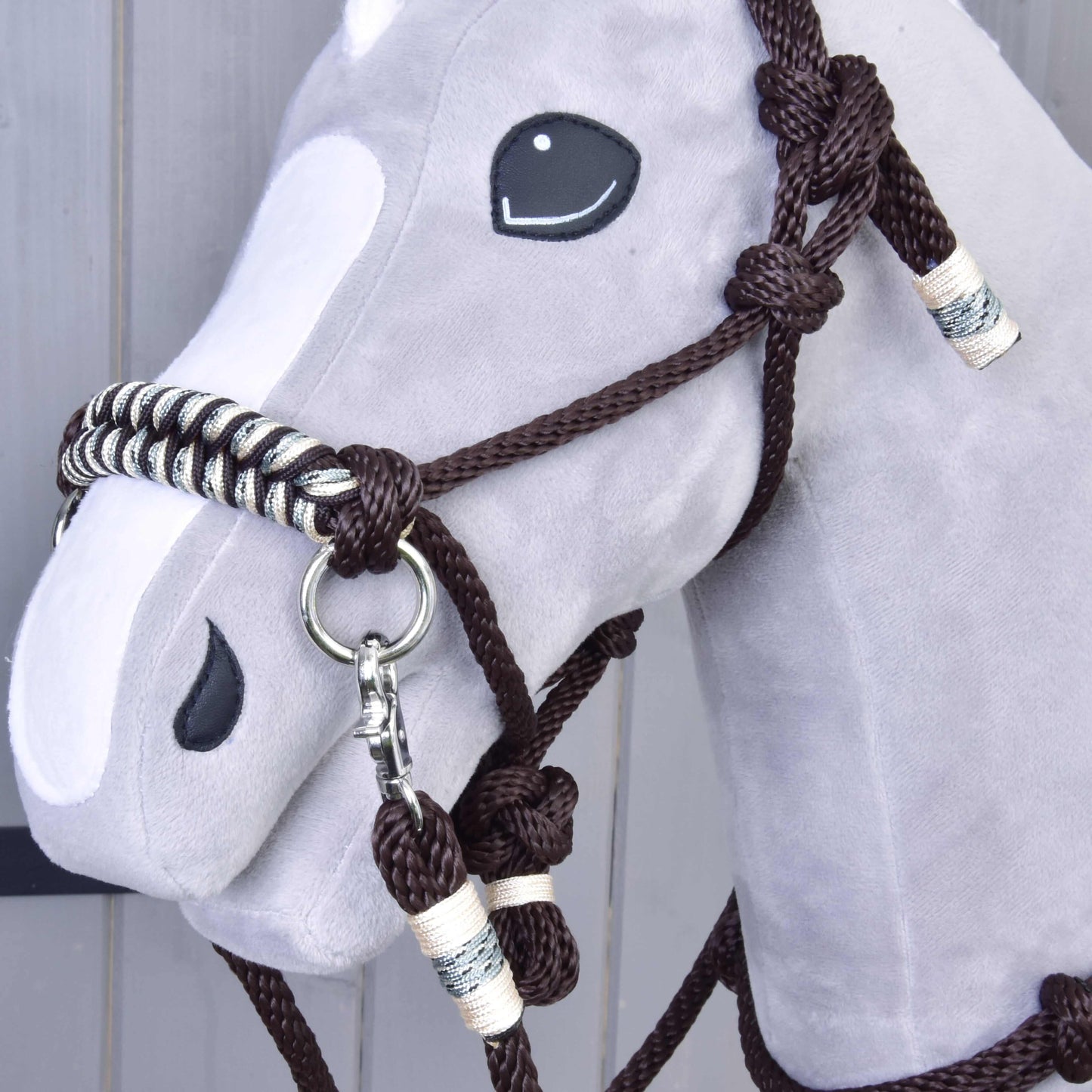 Nahaufnahme eines hellgrau-weißen Hobby Horse Plüschs von Hobby Horse LarDen mit dem Halfter aus dem Seilset Chocolate vor hellem Holzhintergrund.
