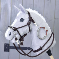 Ein graues Hobby Horse von Hobby Horse LarDen mit Seilset Chocolate mit Halfter für Hobby Horse, Zaumzeug für Hobby Horse und Zügeln steht vor einem hölzernen Hintergrund. Es hat weiße Ohren und eine weiße Mähne sowie ein dekoratives gewickeltes Band am Gesicht.