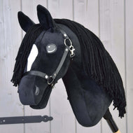 Hobby Horse LarDen „Hobby Horse Cloony mit Schwarzem Halfter“ als plüschiger American Quarter Horse Hengst mit schwarzem Stoff, weißem Gesichtsfleck, Knopfaugen, schwarzer Wollmähne und Zaumzeug vor hellem Holzuntergrund.