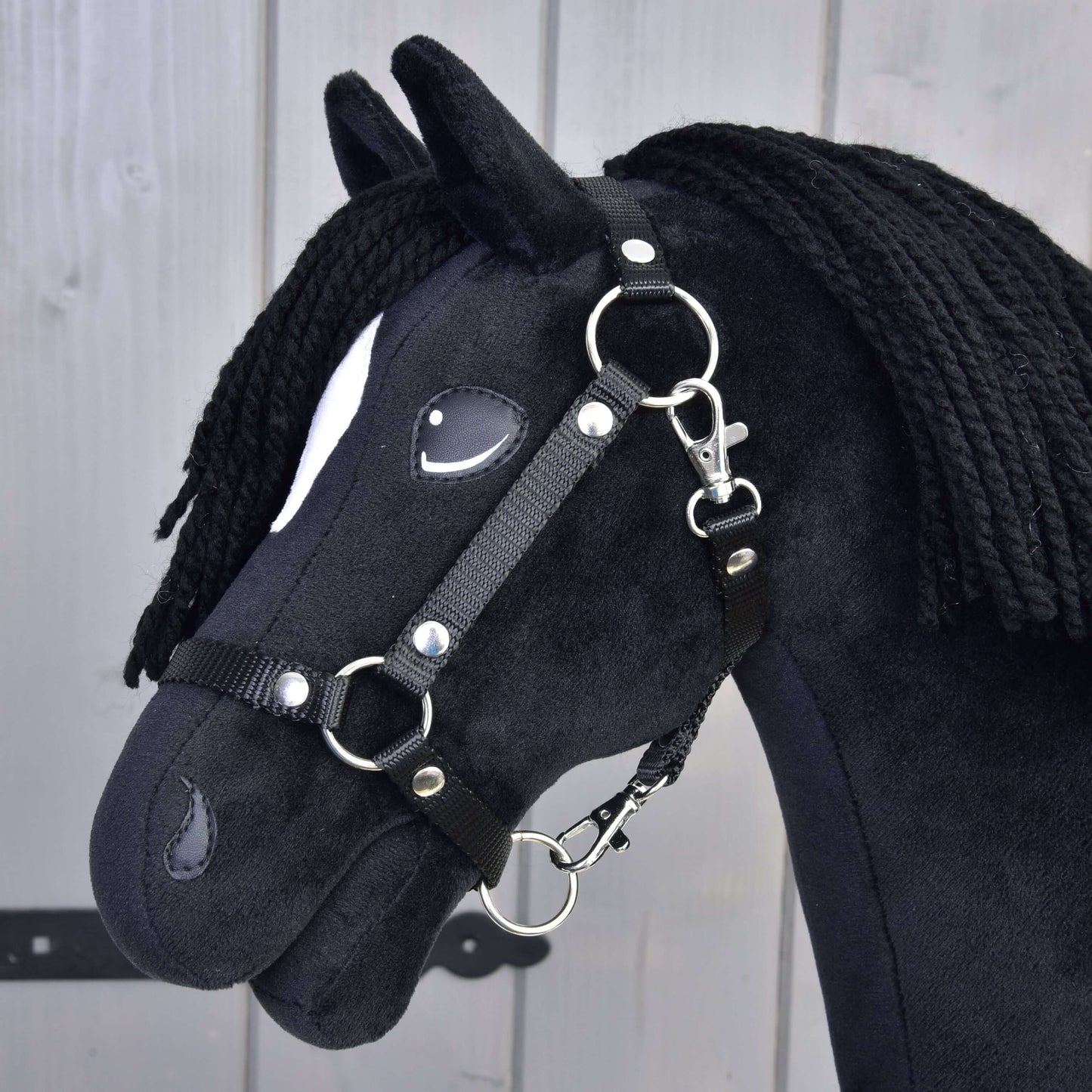Hobby Horse Cloony avec licol noir de Hobby Horse LarDen, cheval noir en tissu au style étalon American Quarter Horse, avec une tache blanche près de l'œil, une crinière noire en fil, photographié sur fond en bois clair.