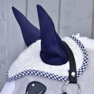 Close-up of a plush horse's head featuring the Hobby Horse LarDen Ear Bonnet Cube Blue on dark blue fabric ears, black harness, and white textured mane with checkered trim. Background: light-colored wooden surface.