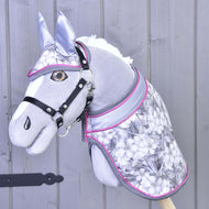 Set Grey Flower von Hobby Horse LarDen mit grauem Plüsch-Hobby Horse, schwarzem Zaumzeug, silber-rosafarbenem Zubehör, Blumenmuster und passender Decke vor hellgrauem Holz-Hintergrund.