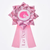 The Hobby Horse Ribbon LarDen Pink, by Hobby Horse LarDen, is a pink horse show ribbon featuring a horse head silhouette in the center and two ribbon tails, with "LarDen" printed on one of the tails.