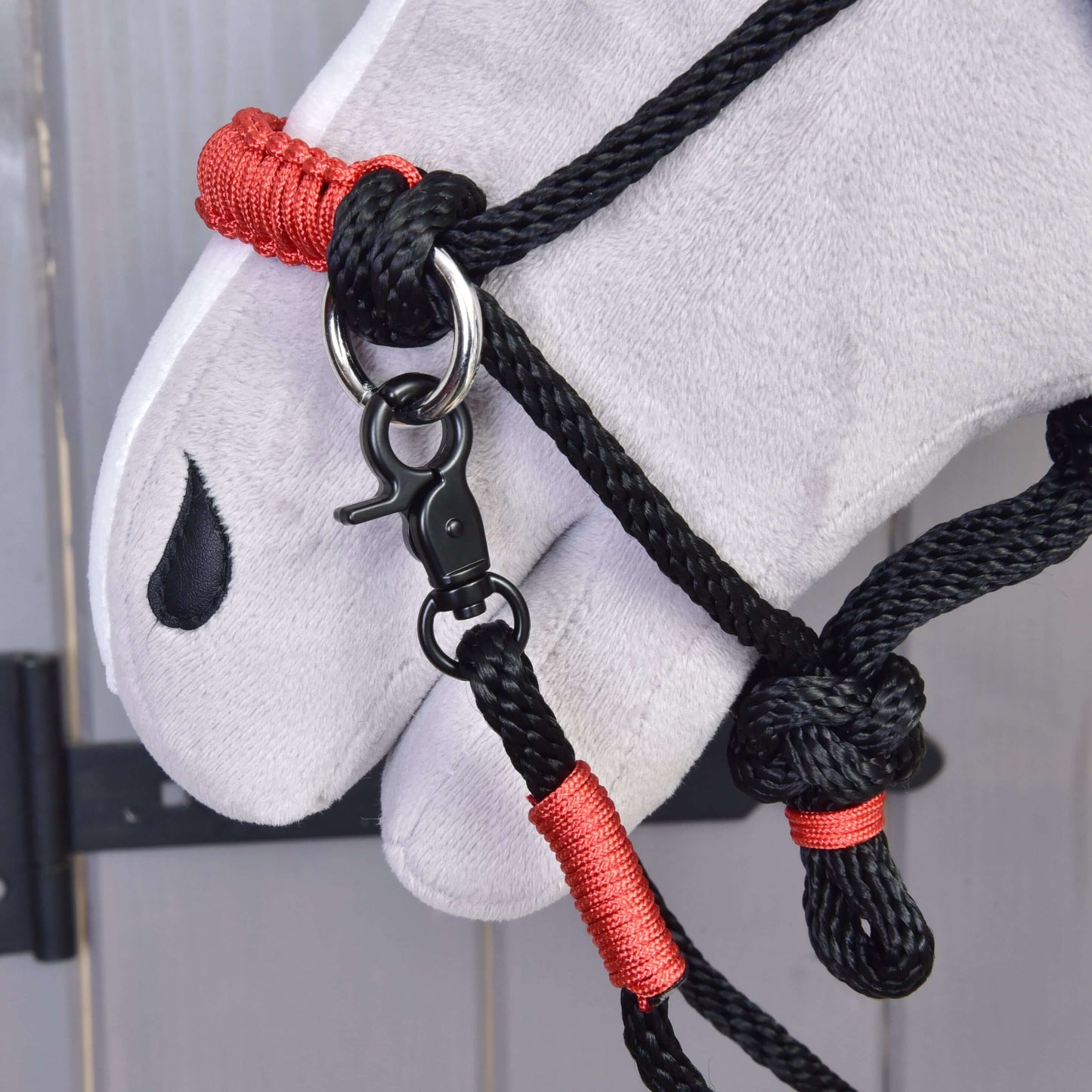 Nahaufnahme eines weißen Plüschpferdekopfes mit dem Halfter des Hobby Horse LarDen Seilset Spark mit roten Bindungen und Metallverschluss sowie einer schwarzen tropfenförmigen Markierung nahe dem Auge.
