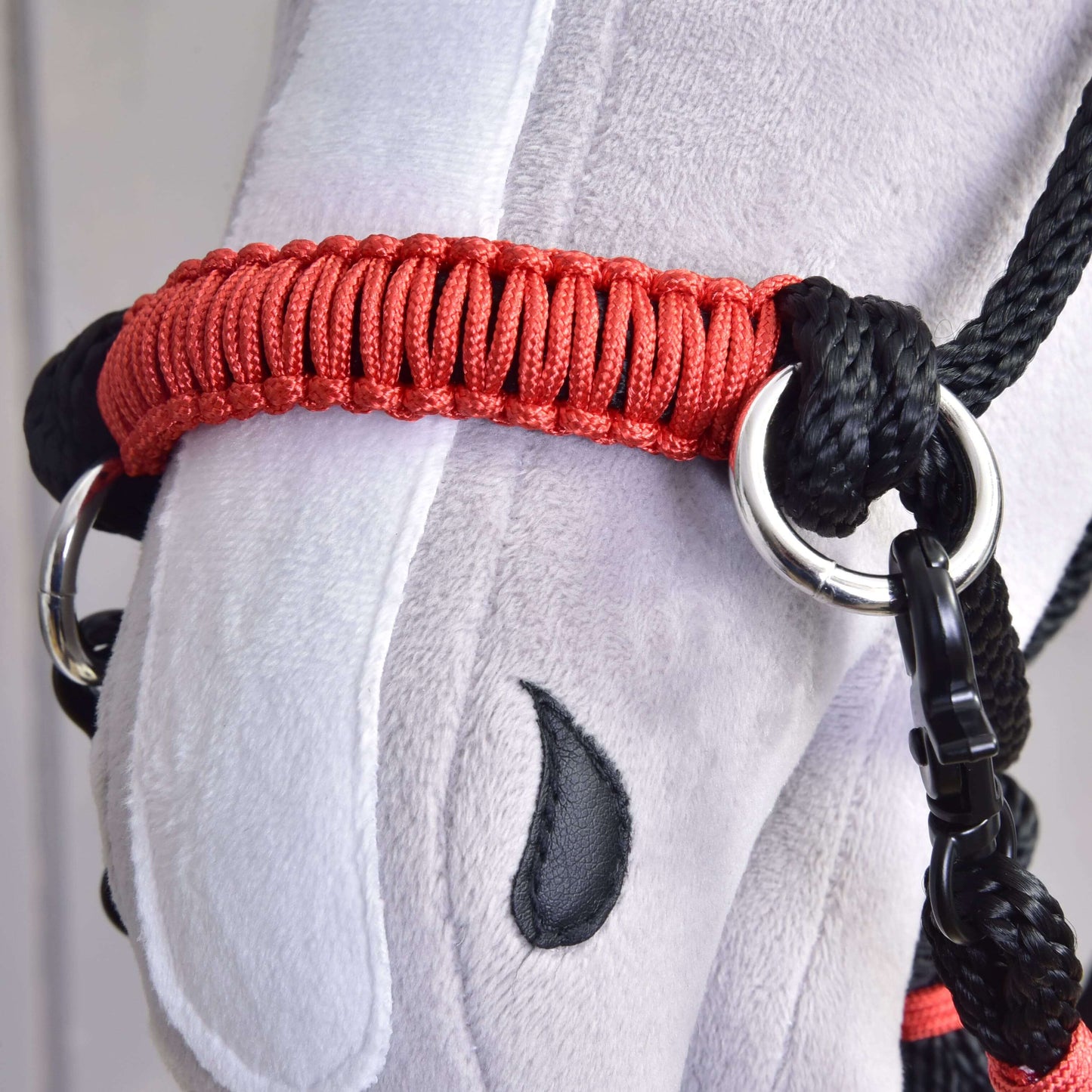Nahaufnahme eines Plüschtier-Pferdekopfes mit rotem und schwarzem Halfter, gesticktem schwarzem Auge und grau-weißem Stoff, mit dem Hobby Horse LarDen Seilset Spark, gefertigt aus robustem Polypropylen als einzigartiges handgefertigtes Accessoire.