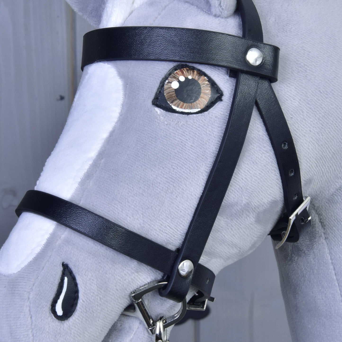 Nahaufnahme des Hobby Horse LarDen Set Basic, eines grau-weißen Plüschpferdes mit detaillierten Nähten, realistisch gesticktem Auge und Nasenloch sowie schwarzem Lederzaumzeug mit Zügeln.