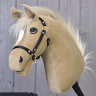 Hobby Horse Dancing Lady mit Schwarzem Halfter von Hobby Horse LarDen, eine beige Plüschstute mit weißer Mähne und weißer Stirnabzeichnung, steht vor einer Wand aus Holzplanken.