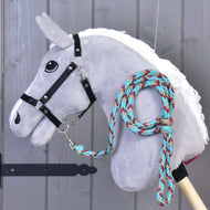 The Hobby Horse LarDen Hobby Horse - Braided lead rope turquise features a gray plush head on a wooden stick, black bridle, and a braided teal, red, and beige lead rope looped around its neck, set against a wooden panel background.