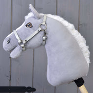 The Hobby Horse LarDen features a gray plush horse with a white mane, brown eyes, and a Halter in light grey leatherette (size S), mounted on a wooden stick and shown against a gray wooden background.