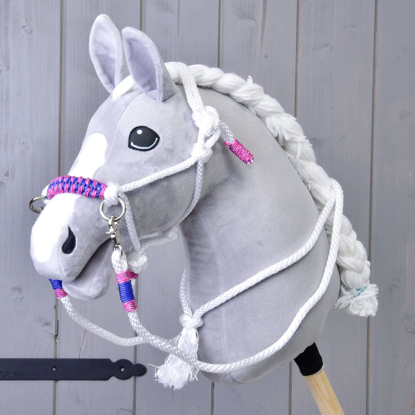 Seilset Weiß (Gr. M) von Hobby Horse LarDen an einem grauen Plüsch-Hobby Horse mit weißer Mähne, Zügeln und geflochtenem Halfter mit rosa und blauen Akzenten vor Holzhintergrund.