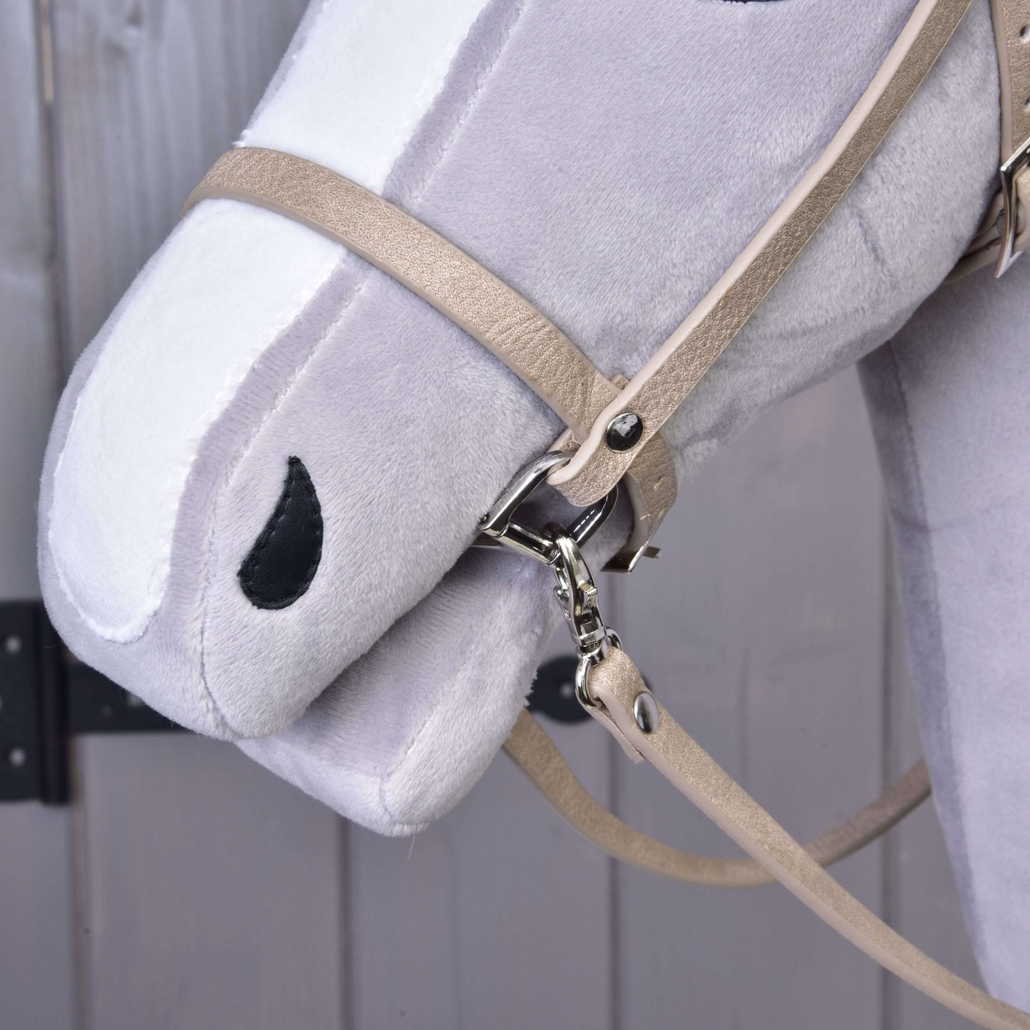 Close-up of a Hobby Horse LarDen plush horse head, featuring the Bordeaux leatherette set—bridle, reins, and martingale—with black-stitched nostril and mouth, shown against a wooden background.