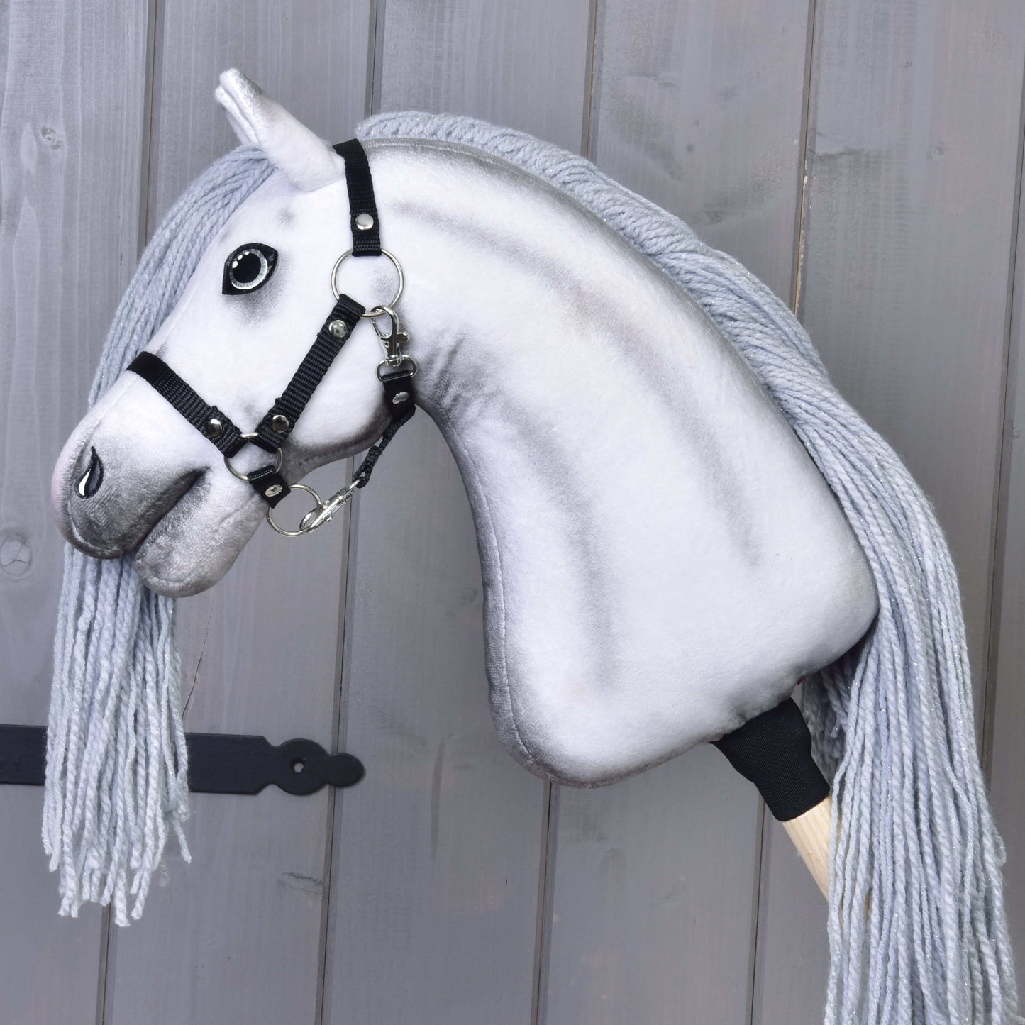 Hobby Horse Einhorn Silver mit Trense und Halfter von Hobby Horse LarDen mit weißem Kopf, schwarzer Trense und Halfter, schwarzen Knopfaugen und langer grauer Mähne vor grauem Holz-Hintergrund.