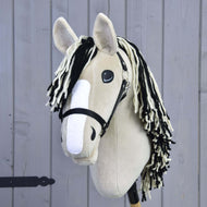 Hobby Horse Aurora mit Schwarzem Halfter von Hobby Horse LarDen mit beigem Plüschdesign, inspiriert vom American Quarter Horse, schwarzem Halfter, schwarz-weißer Garnmähne, weißem Nasenstreifen aus Filz und auf einem Holzstab vor einer hellgrauen Holzwand.