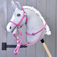 A Hobby Horse LarDen plush gray hobby horse with a white mane is shown featuring the Set Start Pink (halter, cordeo, lead rope, and reins), mounted on a wooden stick against a gray wooden wall.