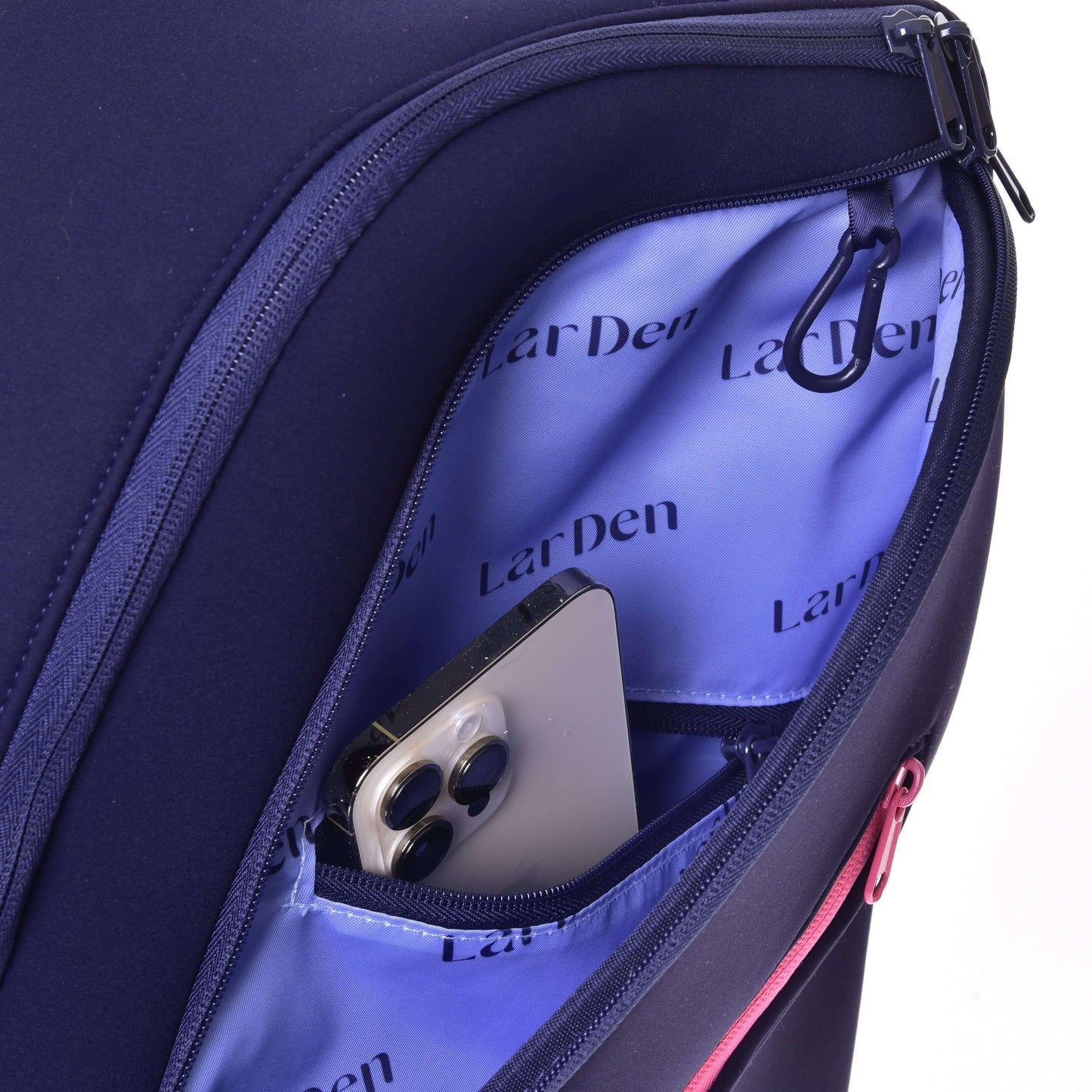 Gros plan sur un sac à dos Hobby Horse LarDen ouvert de Hobby Horse LarDen en néoprène bleu marine avec intérieur violet. Bretelles rembourrées et smartphone avec trois caméras arrière partiellement visible dans la poche intérieure.