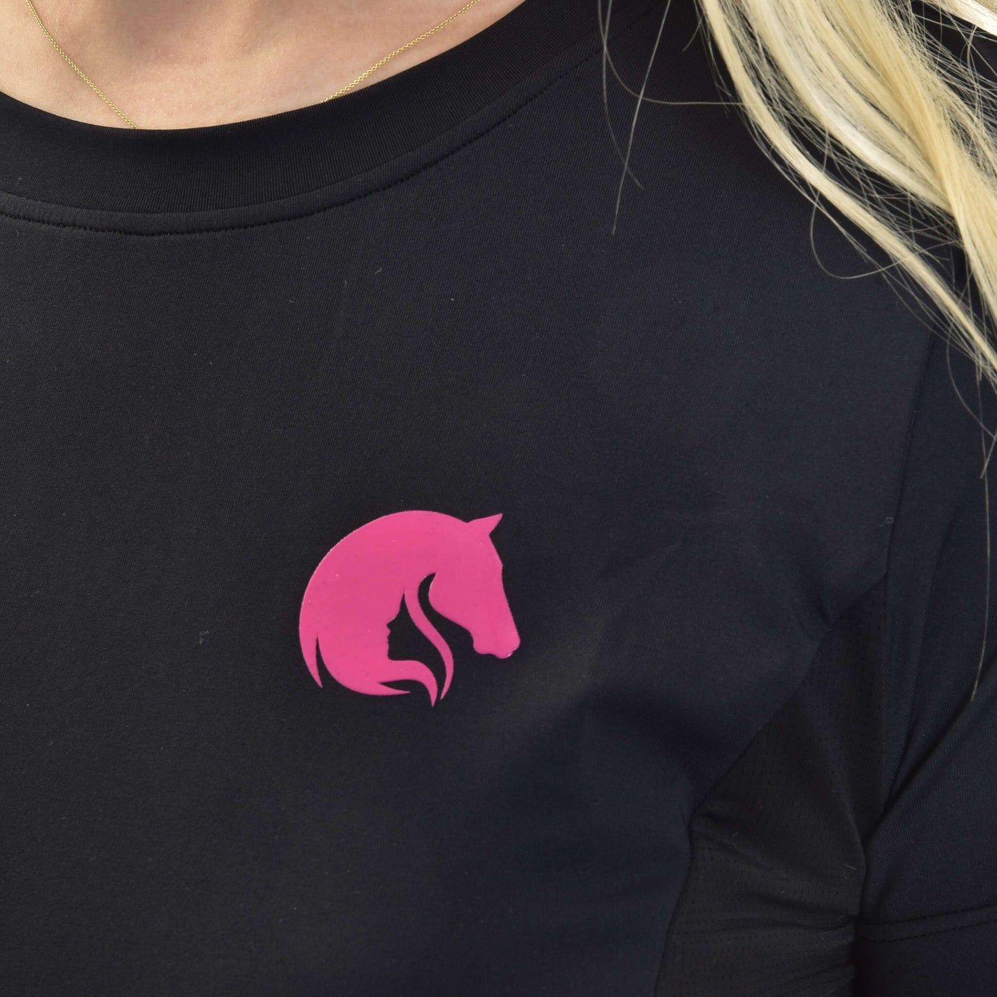 Gros plan d’une personne aux cheveux clairs portant un fin collier en or et le sweat-shirt LarDen de Hobby Horse LarDen, un sweat-shirt noir avec logo tête de cheval rose sur la poitrine.