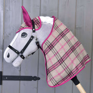 Hobby Horse LarDen Set Cube Pink mit grauköpfigem Stoff-Hobby Horse, schwarzem Zaumzeug und karierter Decke in Beige, Pink und Schwarz vor einer Holzwand.