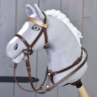 Plüschiges graues Hobby Horse von Hobby Horse LarDen mit weißer Mähne und Hellbraunes Kunstlederset - Zaumzeug, Zügel und Martingale, auf einem Holzstab vor grauer Holzvertäfelung.