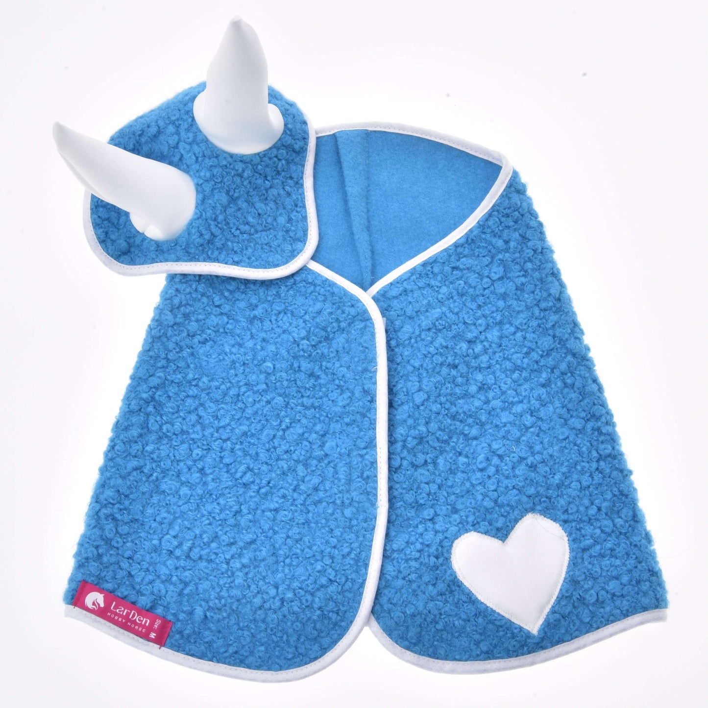 Set Mystery von Hobby Horse LarDen ist eine blaue strukturierte Decke für Hobby Horse mit weißem Besatz, zwei aufrecht stehenden Kragenhörnern, einem weißen Herz-Aufnäher auf einer Seite und einem roten Logo-Etikett am Rand – eine einzigartige Pferdedekoration.