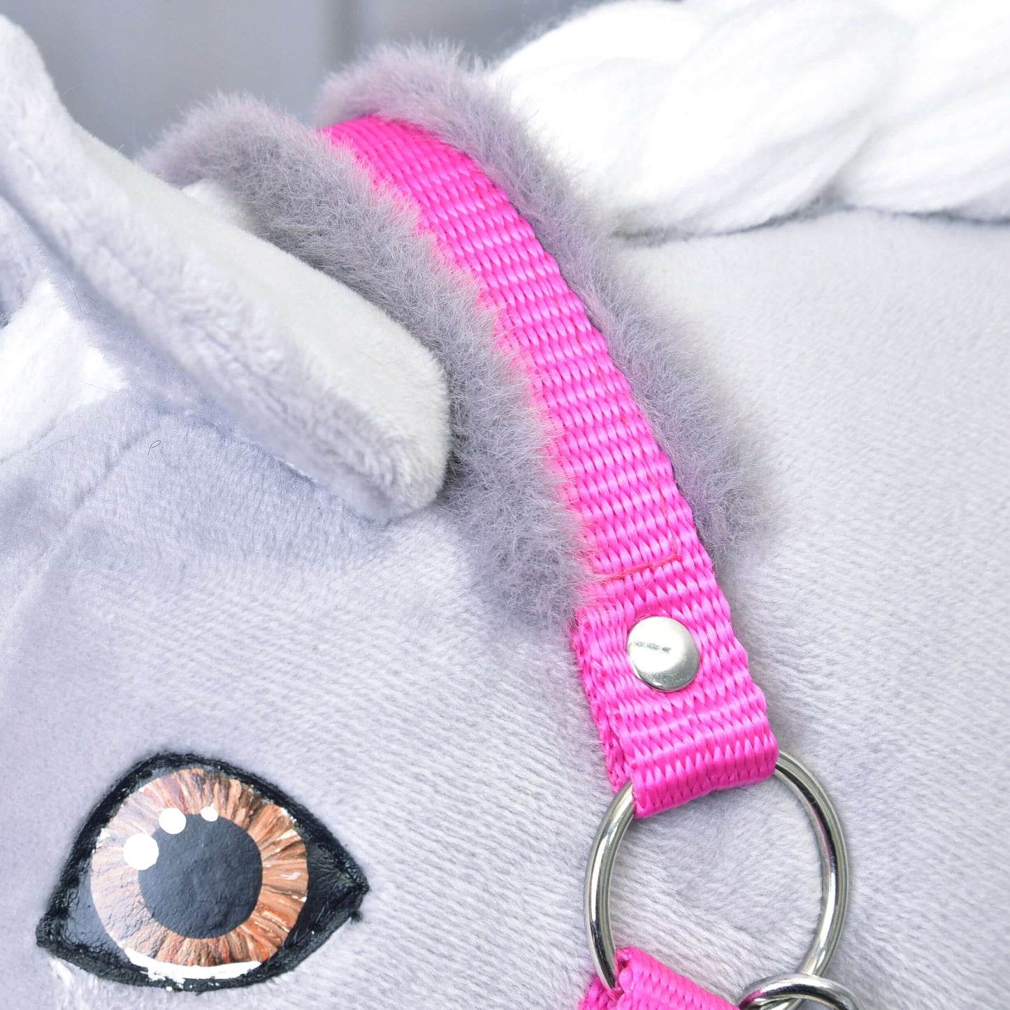 Gros plan sur le Licol rose avec fourrure de Hobby Horse LarDen sur la tête d'un cheval blanc en peluche, avec œil brodé, crinière grise douce et anneau métallique brillant, un adorable accessoire pour le jeu imaginatif avec un Hobby Horse.