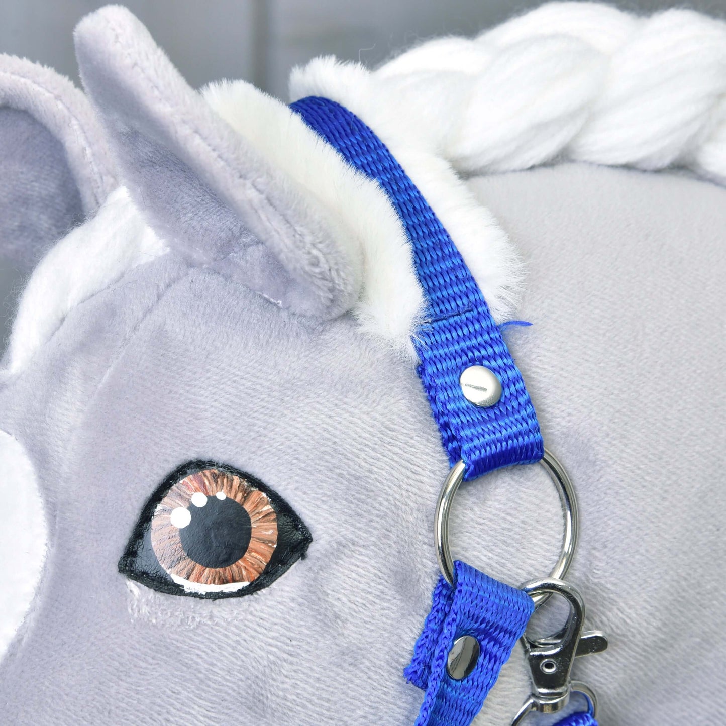 Gros plan sur la tête d'un cheval en peluche avec crinière blanche, portant le Licol bleu avec fourrure de Hobby Horse LarDen. Avec yeux brodés réalistes et tissu gris doux.