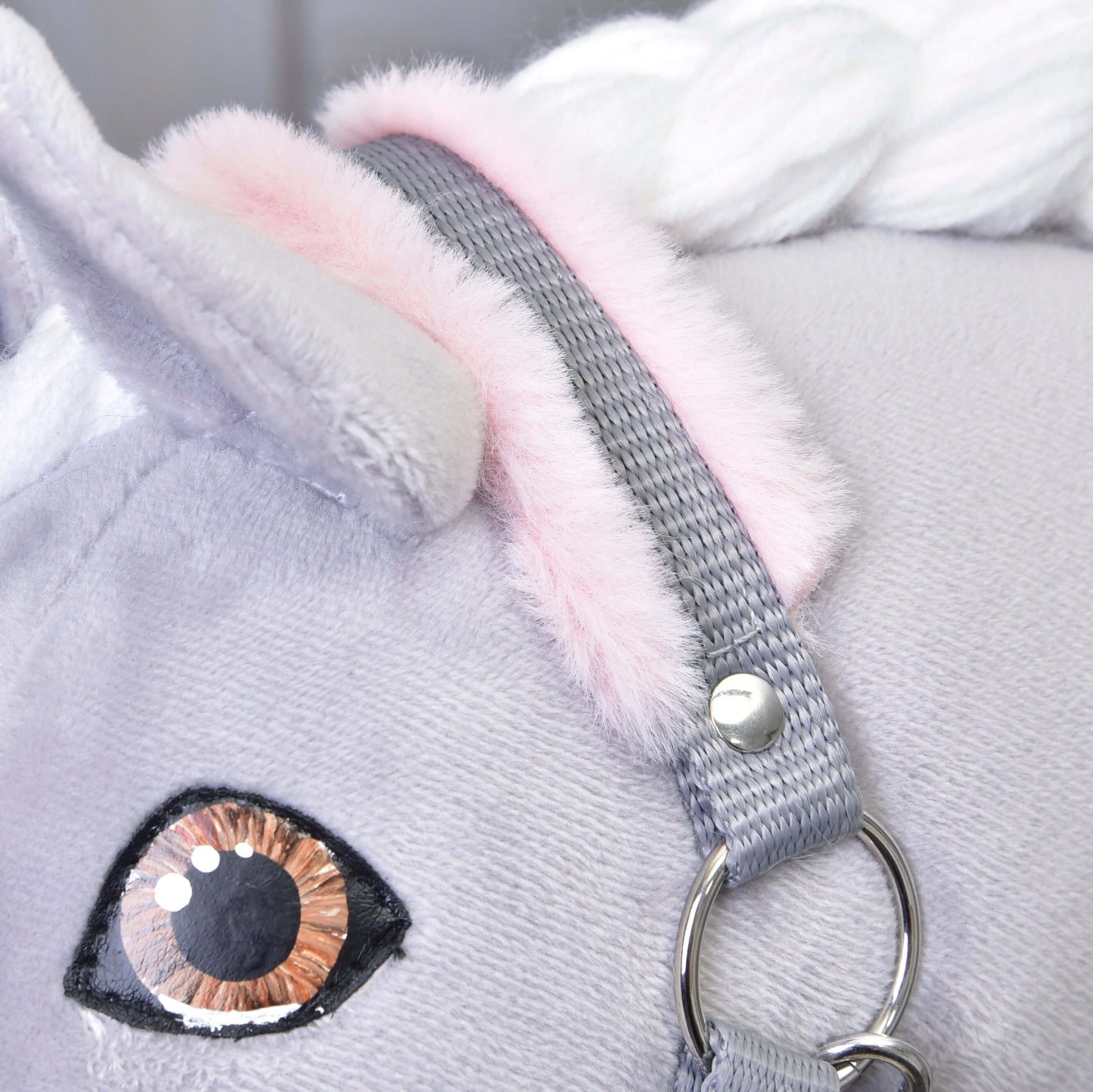 Gros plan sur le Licol gris avec fourrure rose de Hobby Horse LarDen, mettant en valeur son tissu doux gris clair, son oreille intérieure rose, sa crinière blanche tressée et son licol solide avec anneau métallique, un jouet licorne enchanteur et accessoire de cheval fantaisiste.